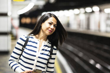 Lächelnde Frau wartet am Bahnhof auf die U-Bahn - WPEF07977