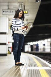 Frau benutzt Mobiltelefon auf dem Bahnsteig einer U-Bahn-Station - WPEF07978