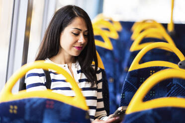 Lächelnde Frau, die im Bus ein Mobiltelefon benutzt - WPEF07999