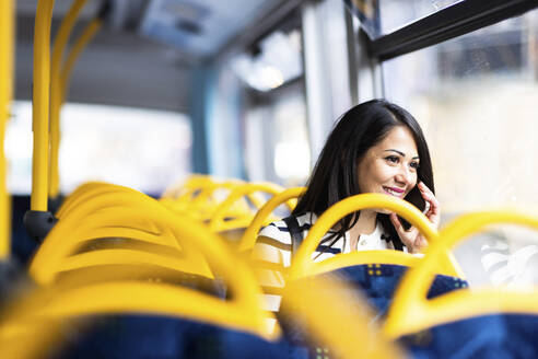 Lächelnde Frau, die mit ihrem Smartphone telefoniert und im Bus reist - WPEF08001