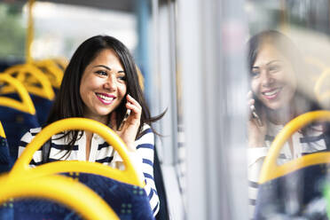 Glückliche Frau, die mit ihrem Smartphone telefoniert und im Bus reist - WPEF08003