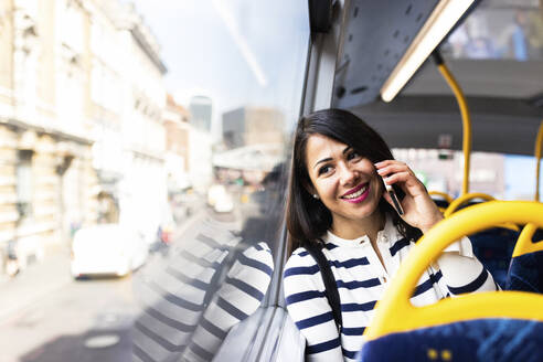 Lächelnde Frau, die im Bus mit ihrem Handy telefoniert - WPEF08004