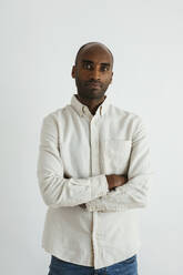 Confident man standing with arms crossed against white background - EBSF04136