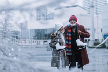 Portrait of seniors with ice skates at outdoor ice skating rink at the winter. Laughing, embracing each other. - HPIF32546