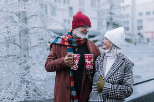 Happy senior couple enjoying outdoor christmas market, driking muled wine. - HPIF32547