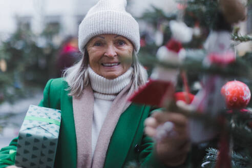 Happy senior woman enjoying outdoor christmas market, buying gifts and Christmas ornaments. - HPIF32554