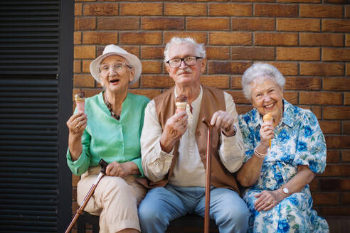 Porträt von drei älteren Freundinnen in der Stadt, die an einem heißen Sommertag Eis essen. Ältere Damen im Sommerurlaub in der Stadt. Rentner auf Gruppenreise. Konzept von Seniorenurlaub und Reisegruppen, Clubs. - HPIF32562