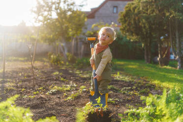 Little boy with a spade working in garden during autumn day. - HPIF32616
