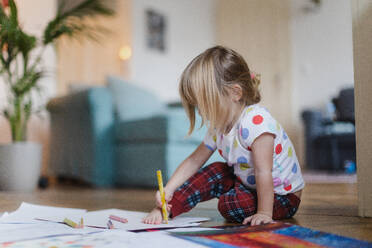 Niedliches kleines Mädchen, das mit Buntstiften auf dem Boden im Wohnzimmer sitzt und ihren eigenen Fuß auf dem Papier skizziert. - HPIF32699