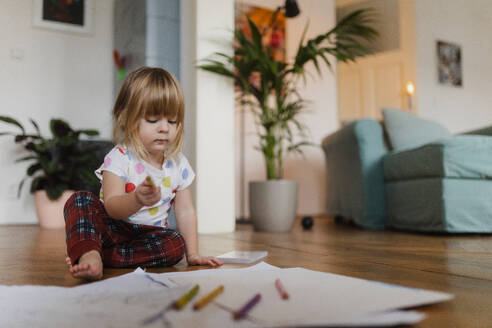 Niedliches kleines Mädchen, das mit Buntstiften zeichnet und auf dem Boden im Wohnzimmer sitzt. - HPIF32703