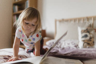 Cute little girl with bangs reading book lying on bed in her child's room. - HPIF32705