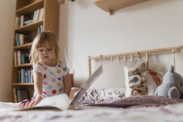 Cute little girl with bangs reading book lying on bed in her child's room. - HPIF32706