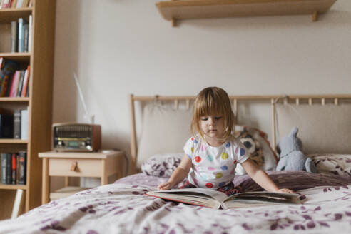 Cute little girl with bangs reading book lying on bed in her child's room. - HPIF32707