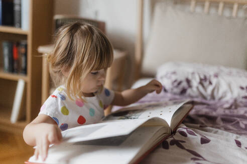 Cute little girl with bangs reading book lying on bed in her child's room. - HPIF32708