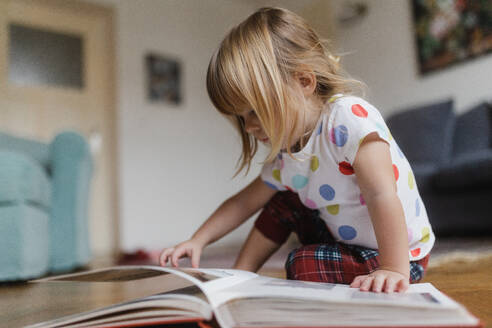 Cute little girl with bangs reading book sitting on the floor in living room. - HPIF32710