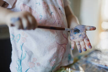 Close up of little girl painting on her own hand with tempera paint, using a paintbrush. - HPIF32714