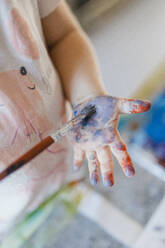 Close up of little girl painting on her own hand with tempera paint, using a paintbrush. - HPIF32715
