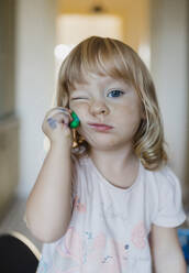 Porträt eines süßen kleinen Mädchens, das mit Spielknete spielt und diese auf der Wange zerdrückt. - HPIF32718