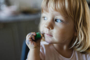 Porträt eines süßen kleinen Mädchens, das mit Spielknete spielt und diese auf der Wange zerdrückt. - HPIF32720