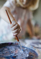 Nahaufnahme einer Kinderhand, die einen Pinsel hält und mit Temperafarbe malt, wobei der Pinsel in die Farbe getaucht wird. - HPIF32723