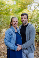 Portrait of happy pregnant woman and her husband, standing in a forest. - HPIF32761