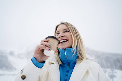 Smiling woman holding coffee cup under sky - MDOF01759