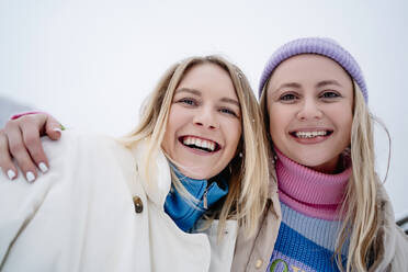 Happy woman with arm around friend under sky in winter - MDOF01764