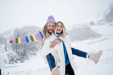 Lächelnde blonde Frau, die ihren Freund auf einem schneebedeckten Berg huckepack nimmt - MDOF01766
