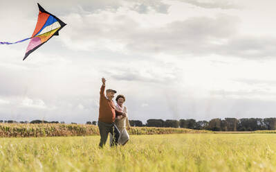 Happy senior couple flying kite in field on sunny day - UUF30713