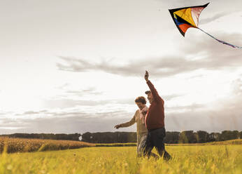 Happy senior couple running and flying kite in field on sunny day - UUF30714