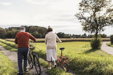 Senior couple with bicycles walking on footpath in field - UUF30716
