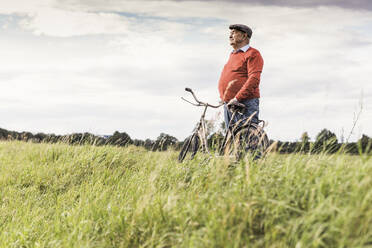 Älterer Mann steht neben einem Fahrrad und betrachtet die Aussicht auf ein Feld - UUF30717