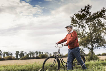 Smiling senior man walking with bicycle in field - UUF30718