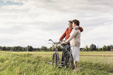 Loving senior couple standing near bicycle under sky - UUF30722