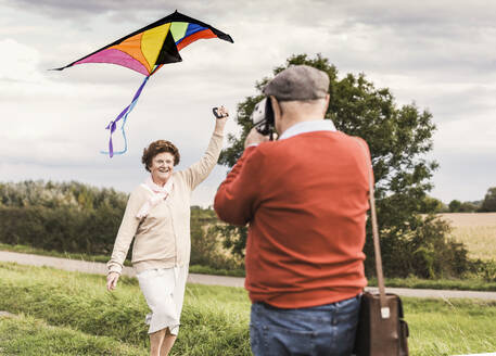 Älterer Mann fotografiert eine Frau, die einen Drachen auf einem Feld steigen lässt - UUF30733