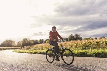 Senior man cycling on road under cloudy sky - UUF30737