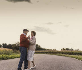Glückliches älteres Paar tanzt auf der Straße unter dem Himmel - UUF30740