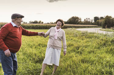 Fröhliches älteres Paar, das sich auf einem Feld vergnügt und tanzt - UUF30741