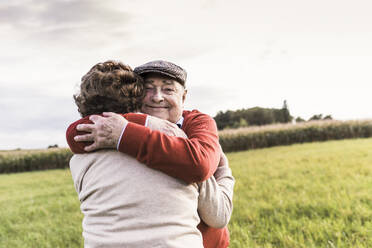 Lächelnder älterer Mann, der eine Frau auf einem Feld umarmt - UUF30742