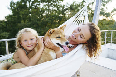 Lächelnde Mutter und Tochter streicheln Shiba Inu Hund in der Hängematte - NJAF00702