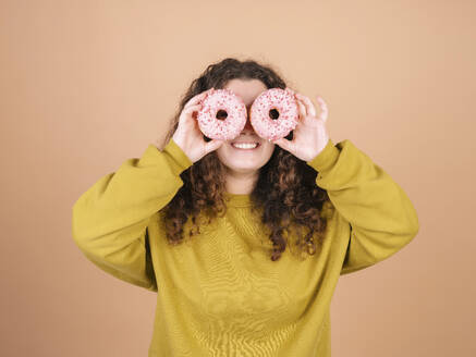 Verspielte Frau hält Donuts über Augen gegen Pfirsich Hintergrund - MMPF01071