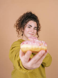 Junge Frau zeigt Donut gegen Pfirsich Hintergrund - MMPF01073