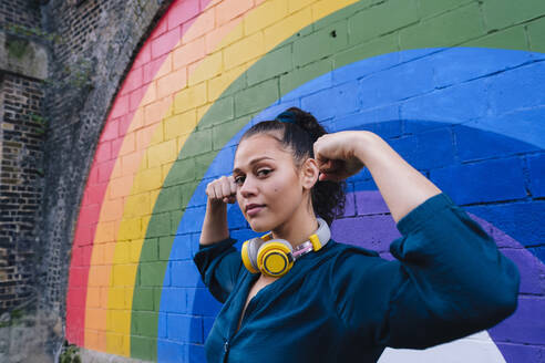 Young woman flexing muscles in front of rainbow wall - ASGF04784