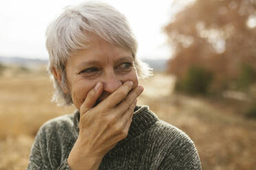 Happy woman with gray hair covering mouth and laughing - EBSF04176