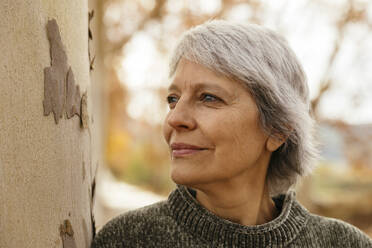 Thoughtful woman with gray hair near tree trunk - EBSF04205