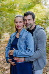 Portrait of happy pregnant woman and her husband, standing in a forest. - HPIF32791