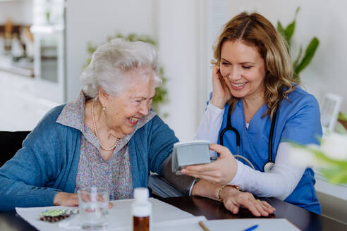 Krankenschwester misst Blutdruck bei einer älteren Frau in ihrem Haus. - HPIF32804