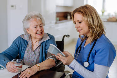 Krankenschwester misst Blutdruck bei einer älteren Frau in ihrem Haus. - HPIF32809