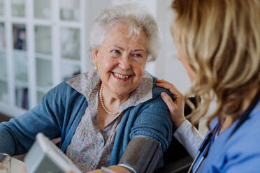 Krankenschwester misst Blutdruck bei einer älteren Frau in ihrem Haus. - HPIF32810