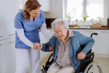 Krankenschwester hilft einer älteren Frau beim Aufstehen aus einem Rollstuhl. - HPIF32834